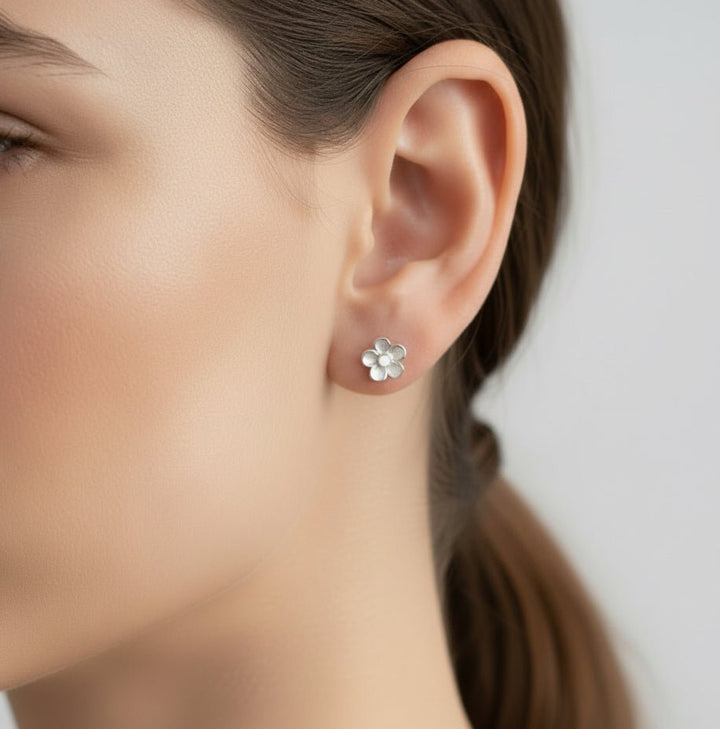 Model wears small forget me not memorial ashes stud earrings made in sterling silver and white resin petals 